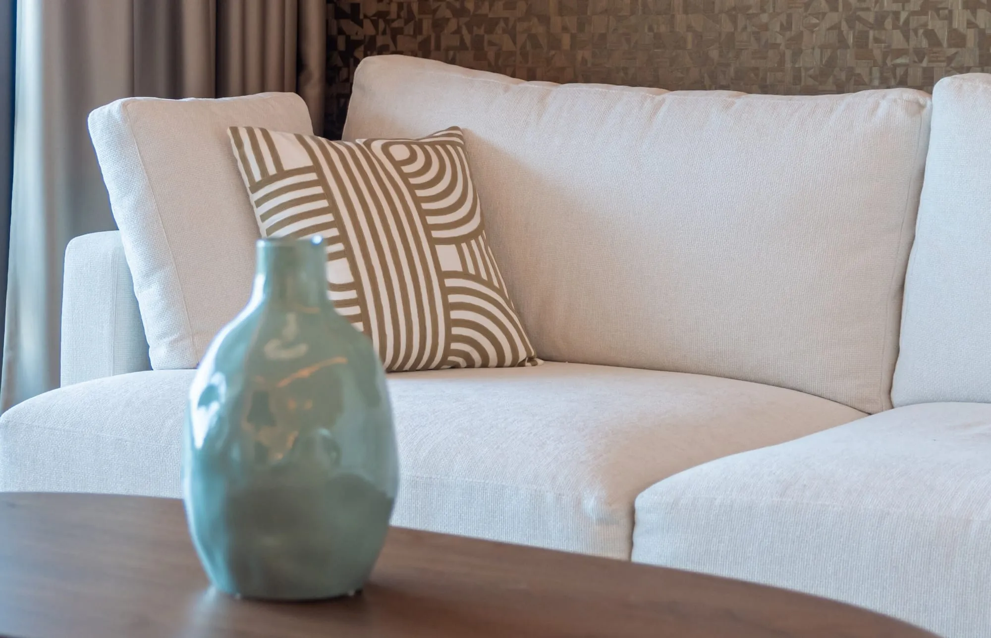 Detail van de hoekbank met een geweven kussen en een turquoise vaas op tafel