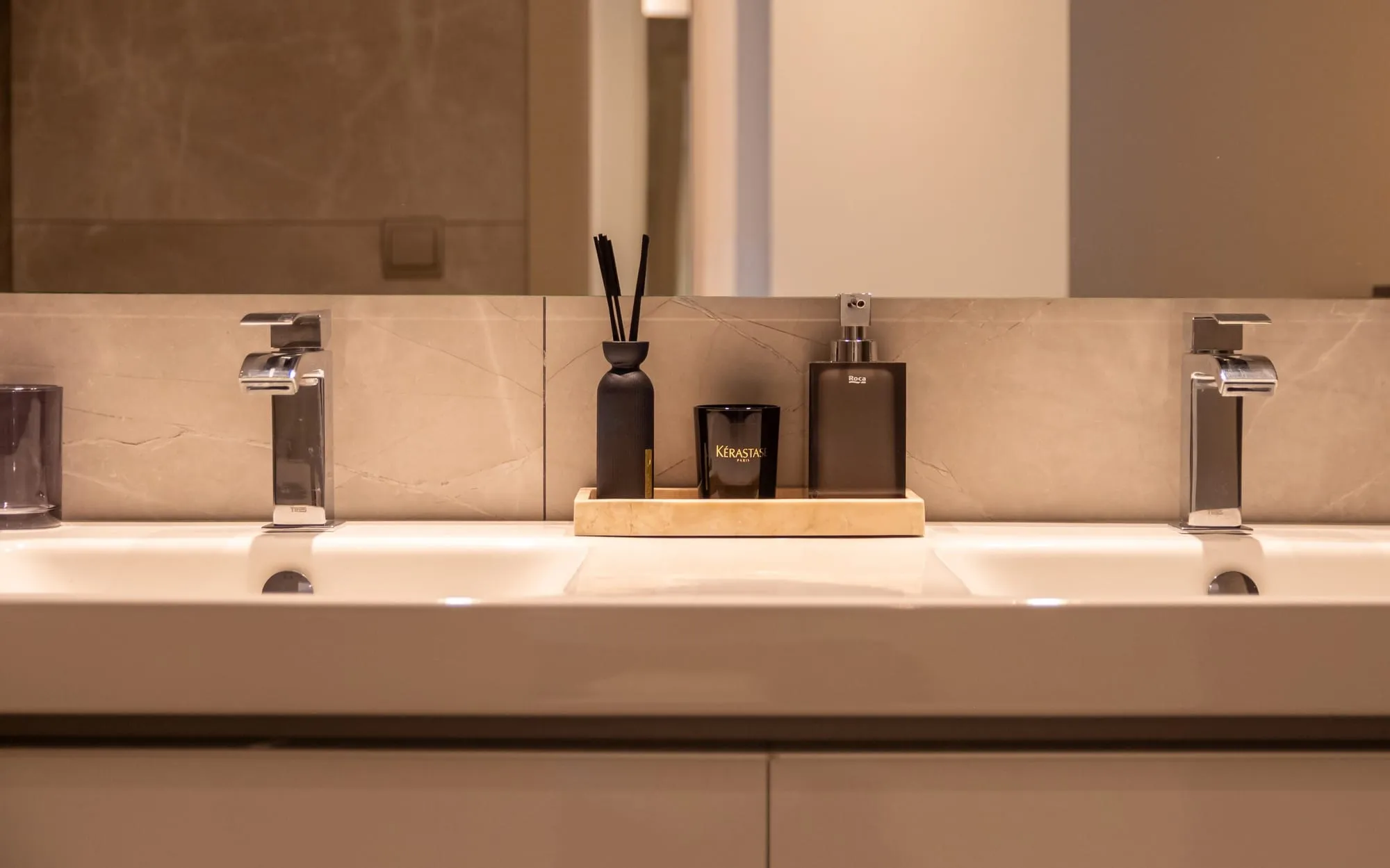 Twee wastafels met kranen in beige marmer, met toiletartikelen op een plateau