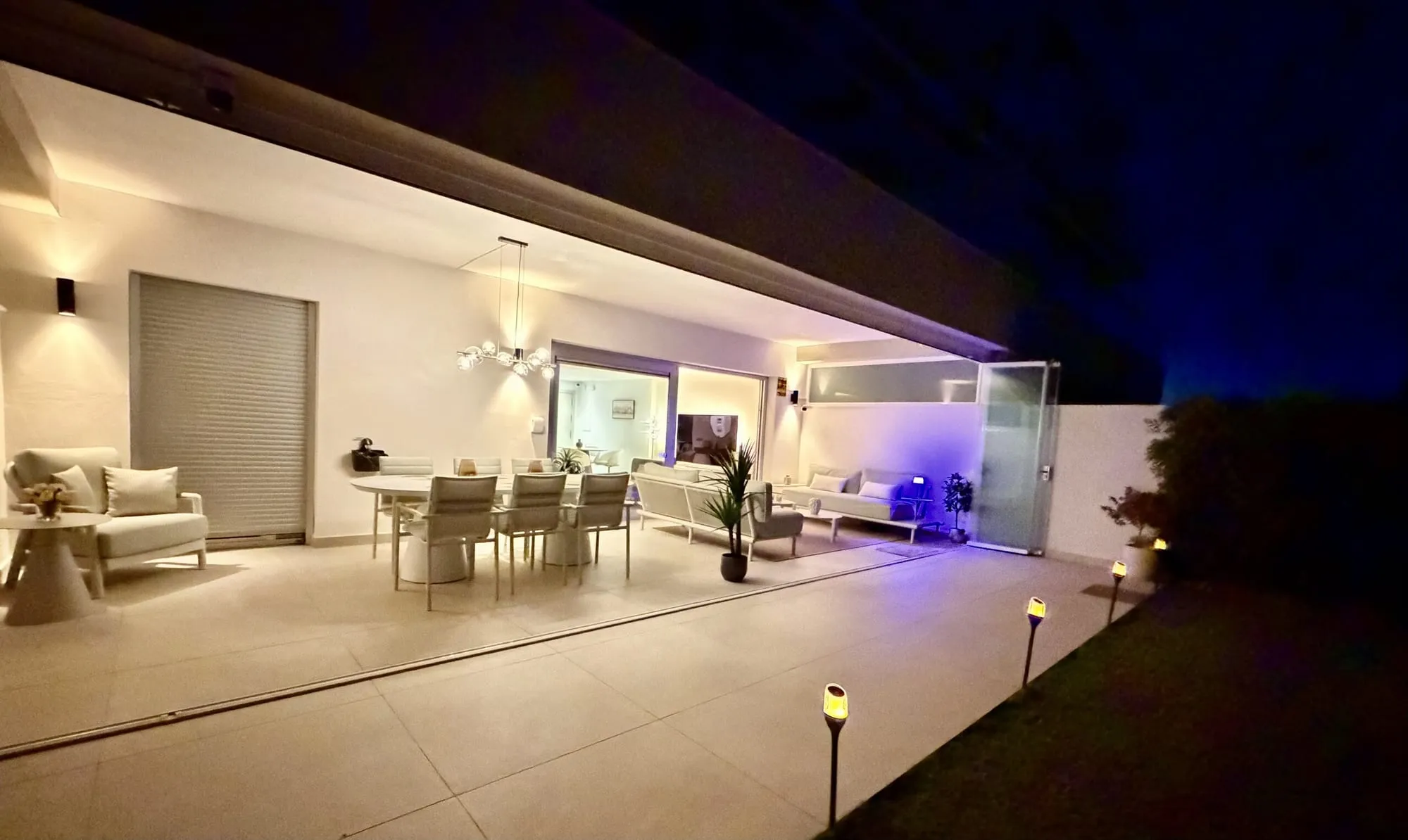 Het verlichte terras bij nacht met de eettafel, en de woonkamer erachter