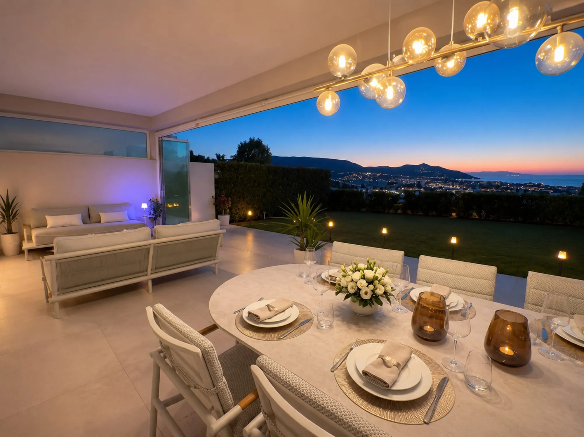 Gedekte tafel op het terras bij zonsondergang, met uitzicht over de bergen en de kust
