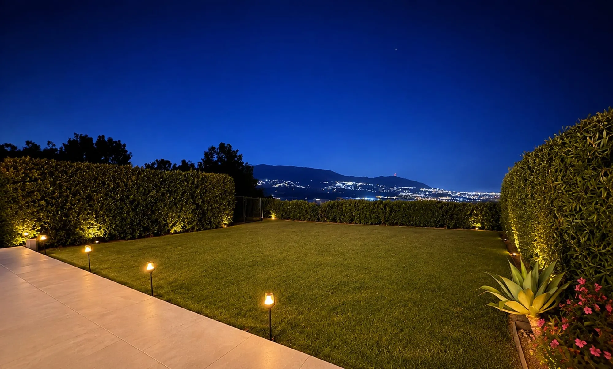 De eigen tuin in de avond, met de lichtjes van de bergdorpen en de kust